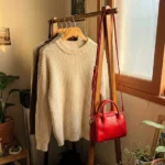 2026년 트렌드 컬러 클라우드 댄서 니트와 레드 미니백이 걸려 있는 자연스러운 방 모습