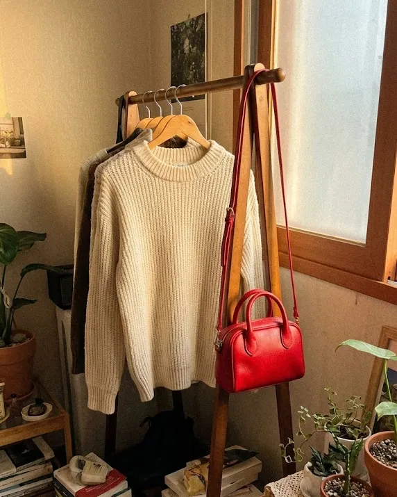 2026년 트렌드 컬러 클라우드 댄서 니트와 레드 미니백이 걸려 있는 자연스러운 방 모습