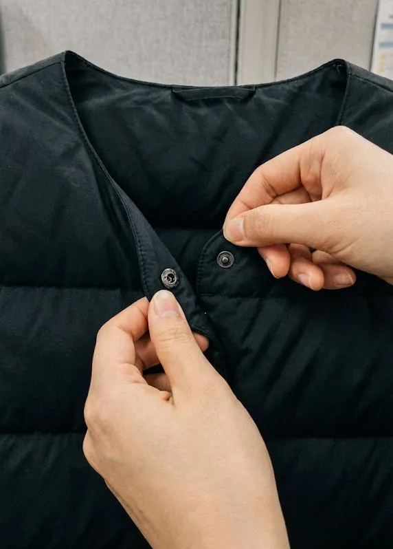 경량패딩 조끼 넥라인을 V넥으로 접어 단추를 채우는 손 클로즈업