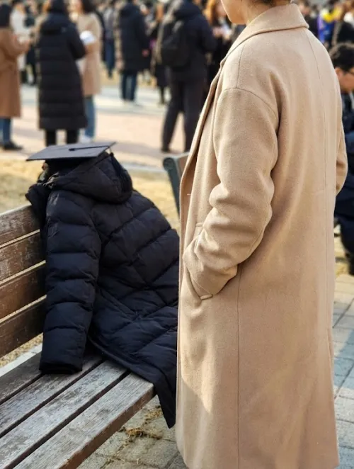 졸업식 야외에서 코트 주머니에 손을 넣고 대기하는 모습