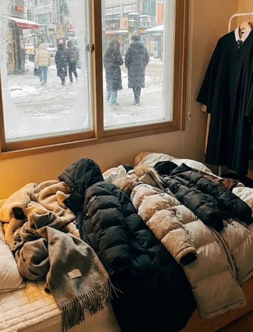 눈 내리는 창밖 풍경과 침대 위 졸업식 코디 고민 흔적