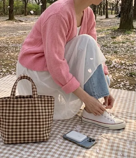 벚꽃 아래 체크 피크닉 가방과 맥세이프 보조배터리가 있는 핑크 가디건 데님 꾸안꾸룩
