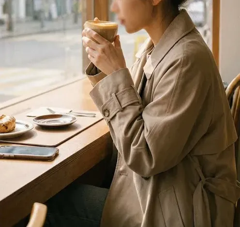 툭 떨어지는 오버핏 베이지 트렌치코트를 입고 커피를 마시는 여성의 자연스러운 측면
