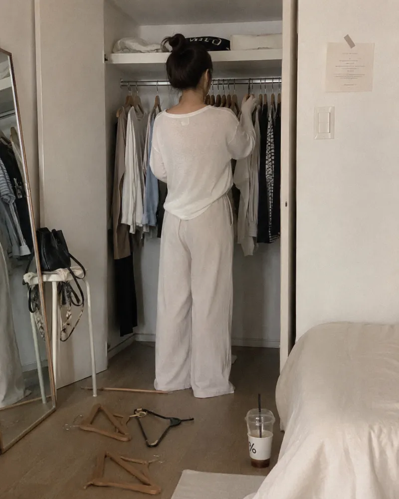 장마 끝난 옷장 앞에서 옷을 고르는 여성의 뒷모습과 흐트러진 옷걸이